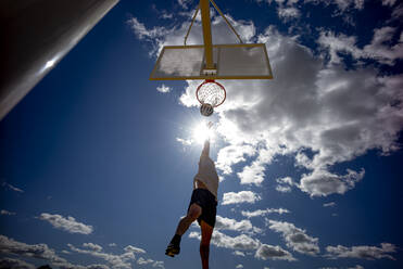 Mann spielt Basketball und dunkt gegen die Sonne - OCMF00847