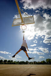 Ein Mann spielt Basketball auf einem gelben Platz und dunkt ein - OCMF00848