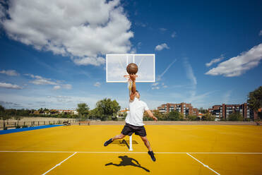 Ein Mann spielt Basketball auf einem gelben Platz und dunkt ein - OCMF00850