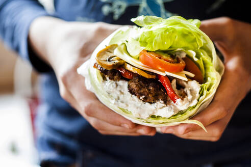 Hände einer Person mit Low-Carb-Burger mit Brötchensalat, gebratenem Gemüse und Tzatziki-Sauce - SBDF04076