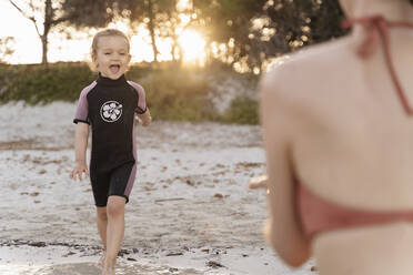 Glückliches Mädchen mit ihrer Mutter am Strand bei Sonnenuntergang - DIGF08722