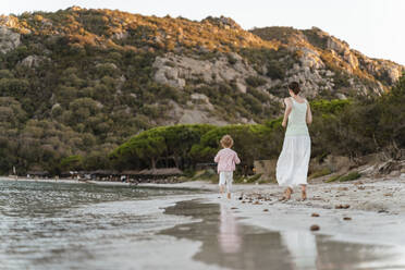 Rückansicht einer Mutter, die mit ihrer Tochter am Strand läuft - DIGF08724