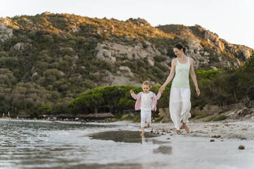Glückliche Mutter, die mit ihrer Tochter am Strand spazieren geht - DIGF08725