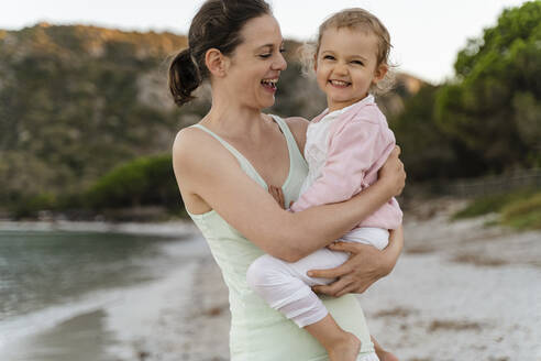 Happy mother carrying her daughter on the beach - DIGF08729