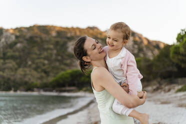 Happy mother carrying her daughter on the beach - DIGF08730