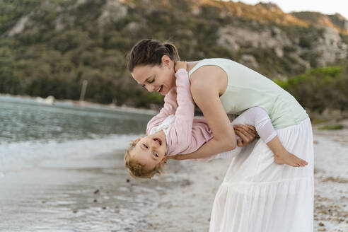 Happy mother carrying her daughter on the beach - DIGF08731