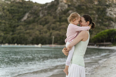 Happy mother carrying her daughter on the beach - DIGF08733