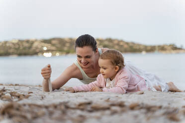 Happy mother and daughter playing with sand on the beach - DIGF08738