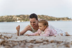 Glückliche Mutter und Tochter spielen mit Sand am Strand - DIGF08738