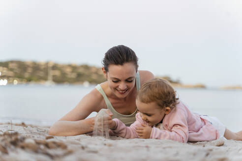 Glückliche Mutter und Tochter spielen mit Sand am Strand - DIGF08740