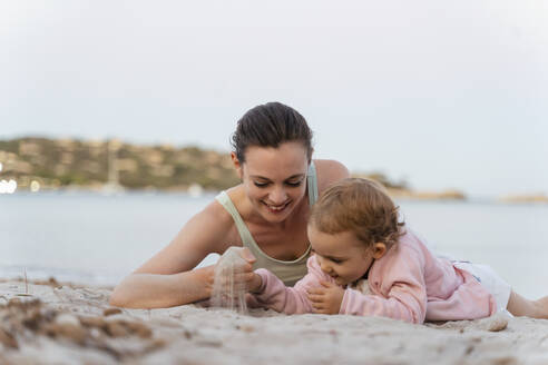 Happy mother and daughter playing with sand on the beach - DIGF08740