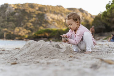 Cute toddler girl playing with sand on the beach - DIGF08744