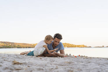 Vater und Tochter spielen mit Sand am Strand - DIGF08757