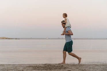 Glücklicher Vater trägt Tochter auf den Schultern am Strand bei Sonnenuntergang - DIGF08758