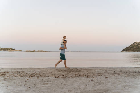 Father carrying daughter on shoulders on the beach at sunset - DIGF08759