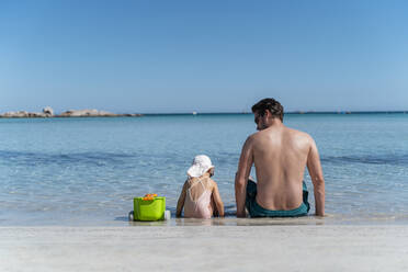 Rear view of father with daughter sitting in the sea - DIGF08762