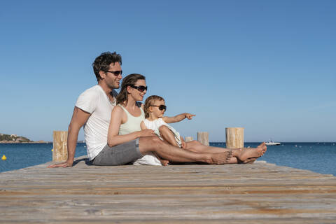 Glückliche Familie auf einem Steg am Meer sitzend, lizenzfreies Stockfoto