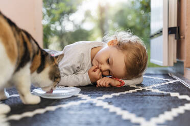 Cute toddler girl watching cat drinking from bowl - DIGF08770