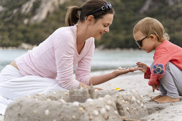 Happy mother and daughter building a sand castle on the beach - DIGF08772