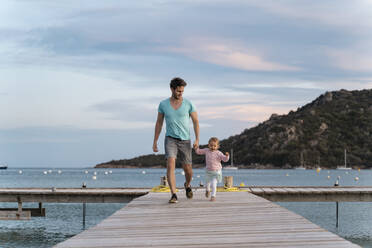 Happy father walking with daughter on a jetty at sunset - DIGF08773