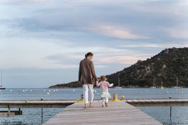 Rear view of mother with daughter walking on a jetty at sunset - DIGF08774