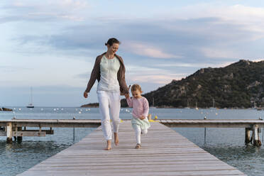 Happy mother with daughter walking on a jetty at sunset - DIGF08775