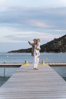 Happy mother carrying daughter on a jetty at sunset - DIGF08776