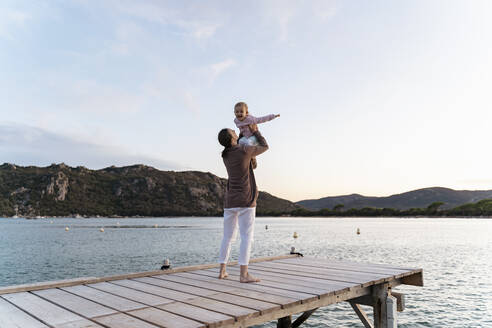 Happy mother carrying her daughter on a jetty at sunset - DIGF08780