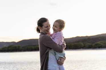 Happy mother carrying her daughter on a jetty at sunset - DIGF08782