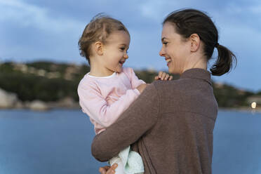 Happy mother carrying her daughter on a jetty at sunset - DIGF08783