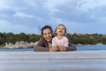Porträt einer glücklichen Mutter und ihrer Tochter, die bei Sonnenuntergang auf einem Steg liegen - DIGF08784
