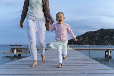 Happy girl walking with mother on a jetty at sunset - DIGF08789