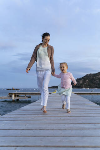 Happy mother with daughter walking on a jetty at sunset stock photo