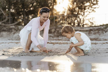 Happy mother with daughter playing with sand on the beach - DIGF08795