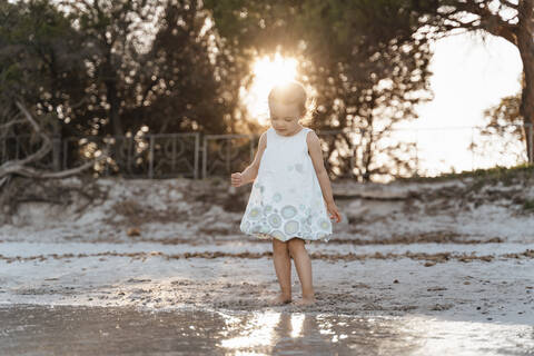 Cute toddler girl standing on the beach at sunset stock photo