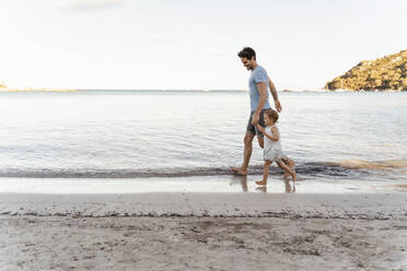 Glücklicher Vater, der mit seiner Tochter am Strand spazieren geht - DIGF08802