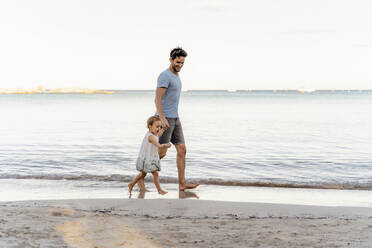 Glücklicher Vater, der mit seiner Tochter am Strand spazieren geht - DIGF08803