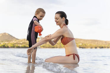 Happy mother and daughter playing with watering can in the sea - DIGF08817