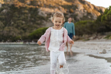 Happy girl running on the seashore with father in background - DIGF08819