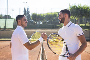 Seitenansicht von zwei Tennisspielern mit Schlägern, die sich vor einem Tennismatch die Hände schütteln und lächeln - ABZF02682