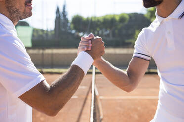 Seitenansicht von zwei Tennisspielern mit Schlägern, die sich vor einem Tennismatch die Hände schütteln und lächeln - ABZF02683