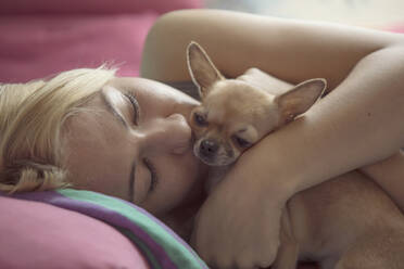 Nahaufnahme eines Teenager-Mädchens, das einen Chihuahua küsst, während es auf dem Bett liegt - CAVF68105