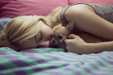 Teenage girl with Chihuahua lying on bed - CAVF68106