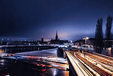 Illuminated railroad track and highway with silhouette church in background during winter - CAVF68137