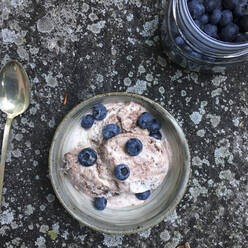 High angle view of blueberries and ice cream in bowl by jar and spoon on rock - CAVF68154
