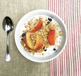 Overhead view of breakfast cereal garnished with peach slices in bowl on table - CAVF68160