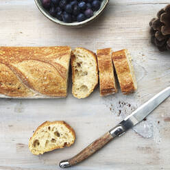 Draufsicht auf Brot mit Messer neben Blaubeeren und Tannenzapfen auf dem Tisch - CAVF68173
