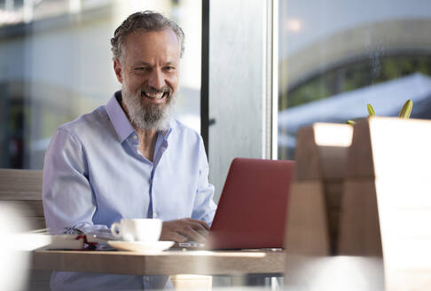 Porträt eines glücklichen reifen Mannes, der einen Laptop in einem Café benutzt - FKF03702