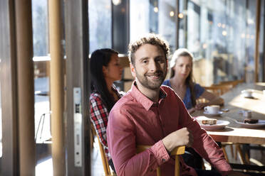 Porträt eines lächelnden Mannes mit Freunden in einem Cafe - FKF03706