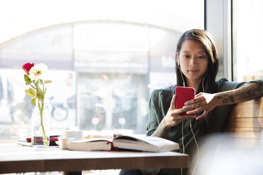 Woman with earbuds and cell phone in a cafe - FKF03710